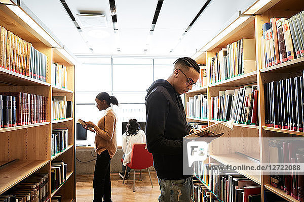 Male and female friends reading book while woman using computer in library at university