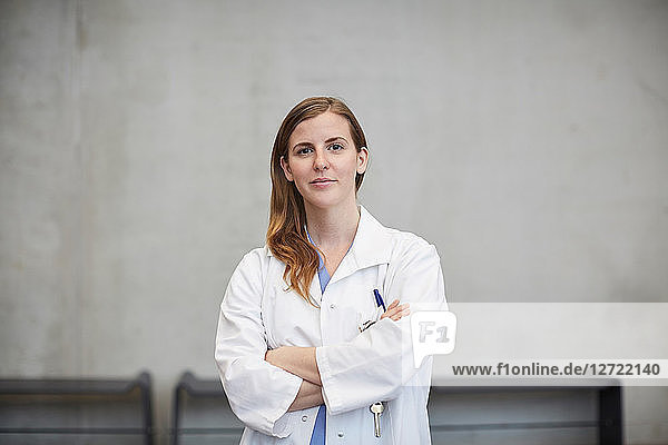 Portrait of confident female doctor standing with arms crossed against wall at hospital