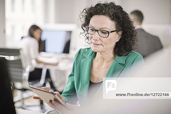 Mature businesswoman using digital tablet while sitting at desk in office