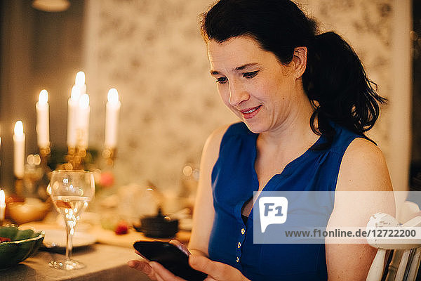 Smiling mature woman using mobile phone at dining table in dinner party