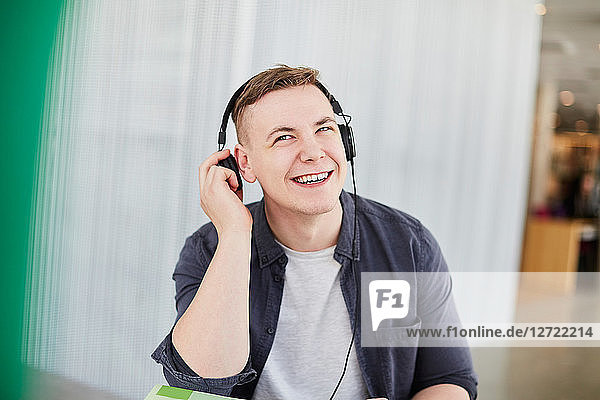 Smiling male student with headphones studying in university cafeteria