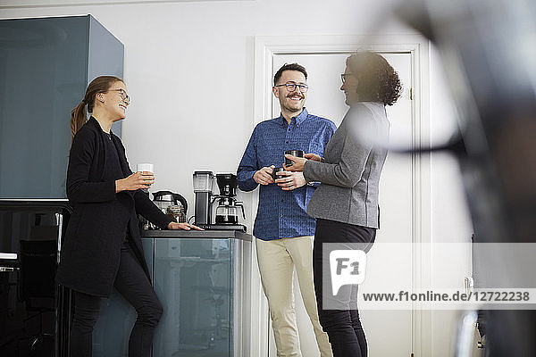 Smiling business colleagues having coffee while talking at office