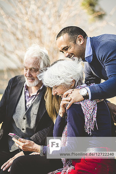 Cheerful multi-generation family looking at mobile phone outdoors