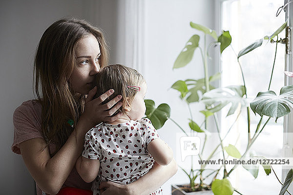 Mother kissing daughter while looking through window at home
