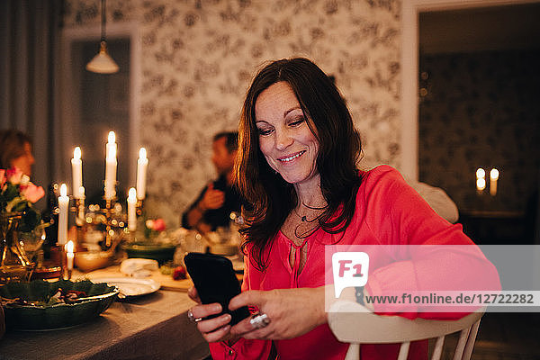 Smiling woman using mobile phone while sitting with friends in dinner party