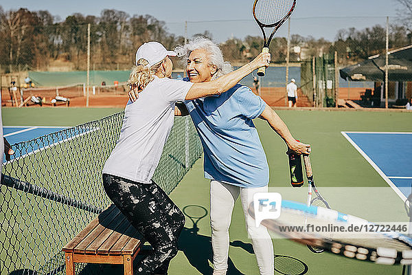 Happy female senior friends greeting at tennis court during summer