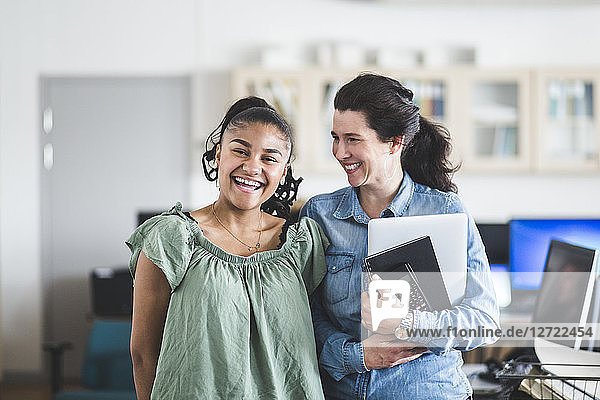 Portrait of smiling teenage student standing with teacher in computer lab at high school