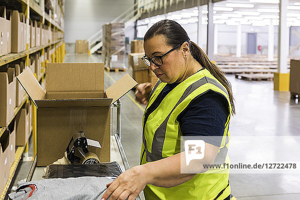 Side view of female worker packing cardboard box at warehouse