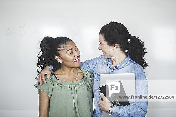 Smiling teenage high school student looking at teacher standing against whiteboard in computer lab