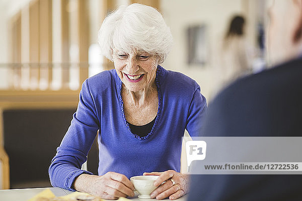 Senior woman smiling while having drink at table with man in nursing home