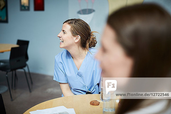 Smiling female medical workers looking away while sitting at table in hospital cafeteria