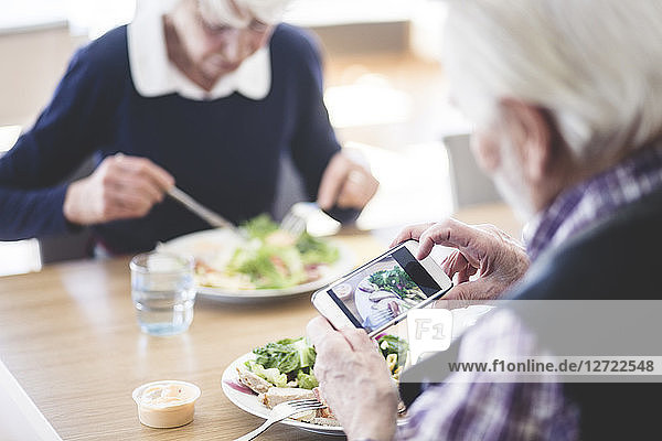 Senior man photographing food using smart phone while having lunch with woman at table