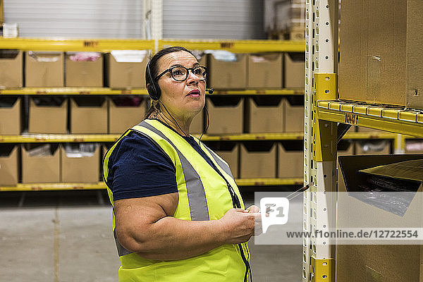Mature female worker with digital tablet looking away while talking on headset at distribution warehouse