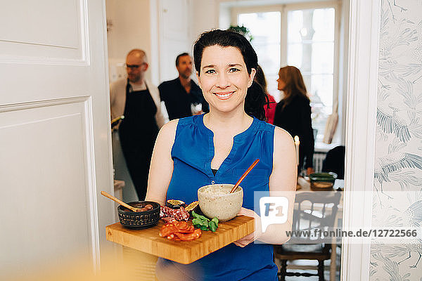 Portrait of smiling woman holding serving tray while standing at doorway in party