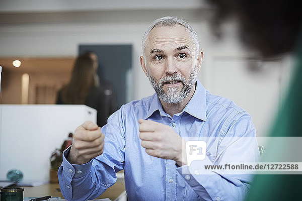 Mature financial advisor gesturing while explaining female colleague at desk