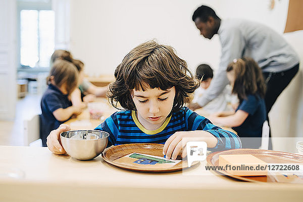 Boy looking at plate on table against friends and teacher in classroom