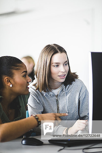 Multi-ethnic teenage girls discussing over computer monitor at desk in classroom