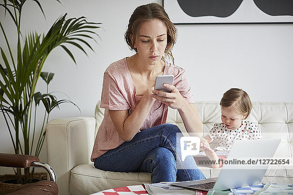 Fashion designer using mobile phone while sitting with daughter on sofa at home