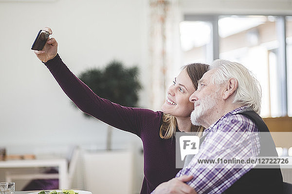 Young woman taking selfie with grandfather while sitting in nursing home