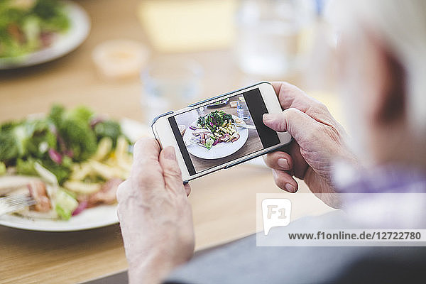 Cropped image of senior man photographing food through mobile phone at table