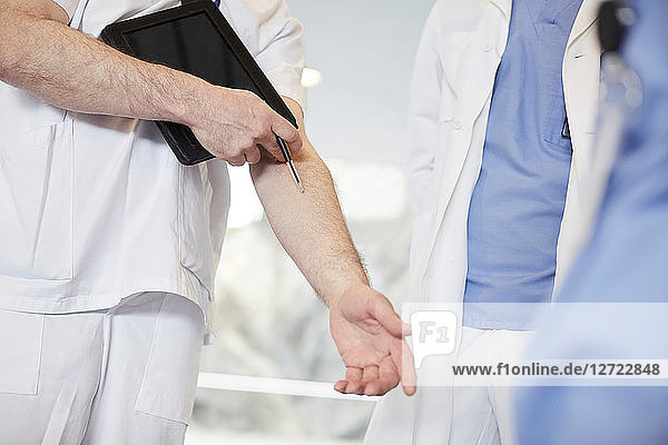Midsection of male nurse gesturing while standing with coworkers at hospital