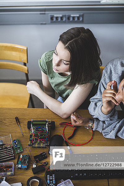 High angle view of female teenage students sitting with robot at desk in classroom