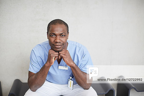 Portrait of confident mid adult male nurse sitting against wall at hospital