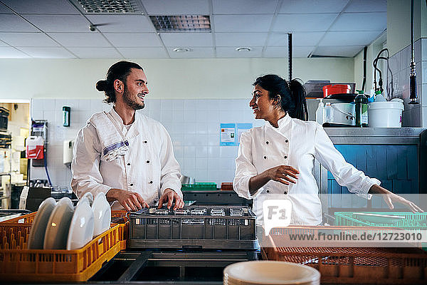 Male and female chefs communicating while arranging utensils in kitchen