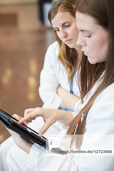 Confident female doctors discussing over digital tablet in corridor at hospital