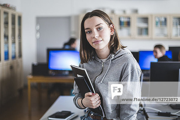 Portrait of confident high school female student with books in classroom