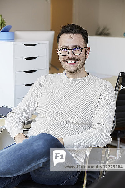 Portrait of smiling businessman sitting on chair at office