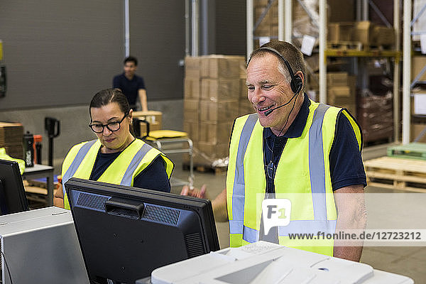 Confident senior male customer service representative talking through headset while standing by coworker in distribution