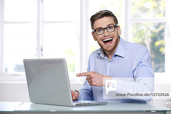 Mann in blauem Hemd  Brille  Bart  lächelnd  Fenster im Hintergrund unscharf  sitzend  tippt auf einem Computer-Laptop