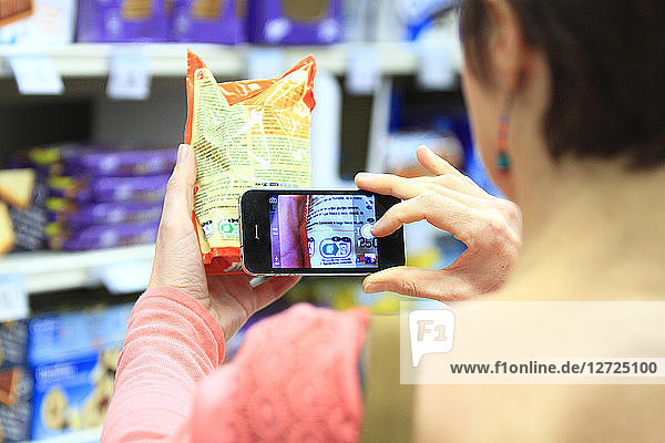 woman in a supermarket photographing a product with its smartphone.
