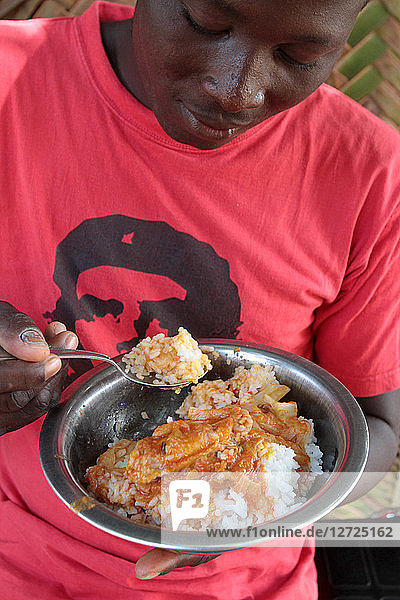 Ein togolesischer Teenager isst eine Schüssel Reis mit Huhn. Lome. Togo. /