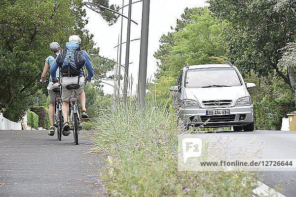Frankreich  Pyla sur Mer  Ocean Boulevard  Fahrradweg  ein radelndes Paar auf einem Fahrradweg  ein Auto gegen den Sinn  eine Allee aus Grün