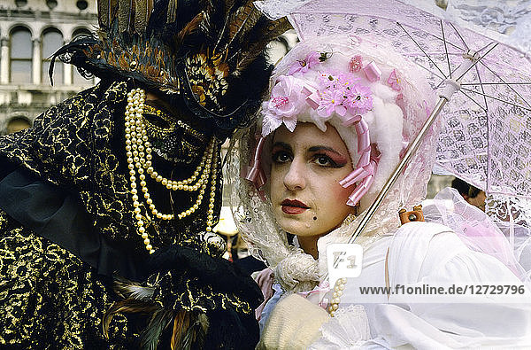 Europa  Italien  ein Paar mit Maske im Karneval von Venedig. Ein maskierter Mann mit einem goldenen Wolf und einer Perle. Eine Frau in weiß gekleidet trägt einen rosa Regenschirm