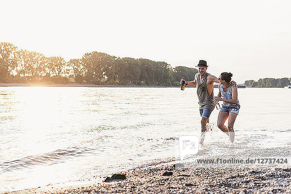 Happy young couple wading in river at sunset