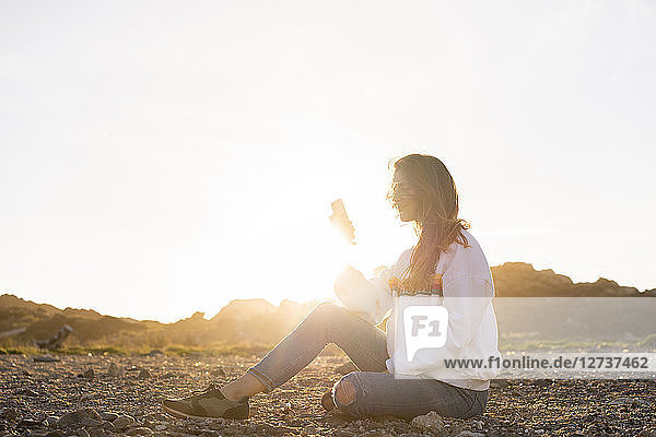 Young woman at the beach  using smartphone at sunset