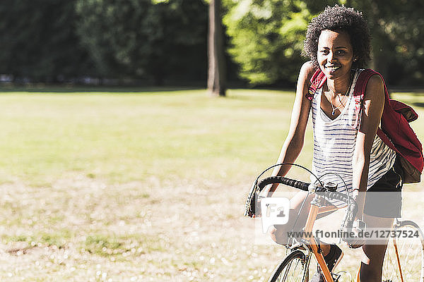 Portrait of smiling young woman on bicycle in park