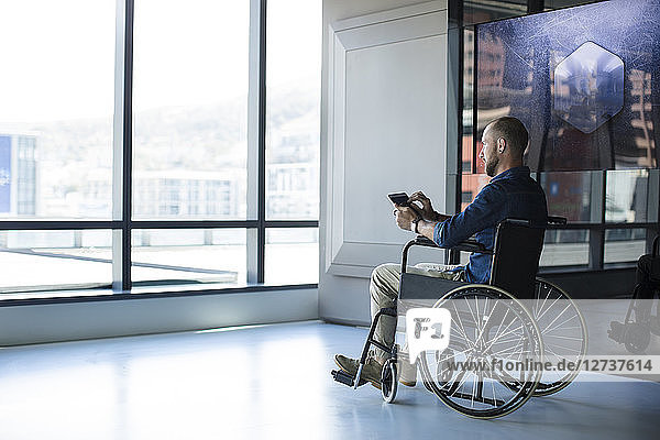 Man in wheelchair looking out of window in office  using tablet