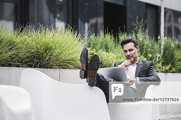 Relaxed businessman using laptop outside office building