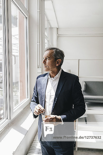 Mature businessman with glass of coffee in his office looking out of window
