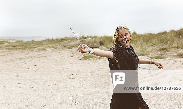 Spain  Aviles  happy teenage girl holding a sparkler on the beach
