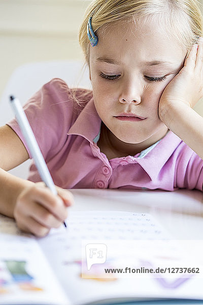 Portrait of bored little girl writing numbers in exercise book