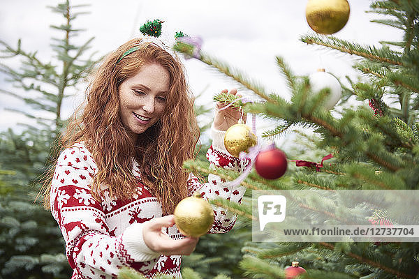 Portrait of redheaded young woman decorating Christmas tree outdoors