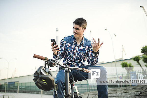 Young man with bicycle looking at smartphone and gesturing