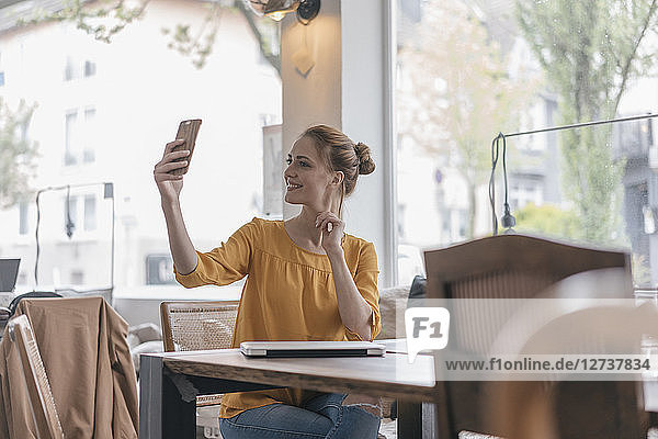 Young woman sitting in coworking space  taking smartphone selfie