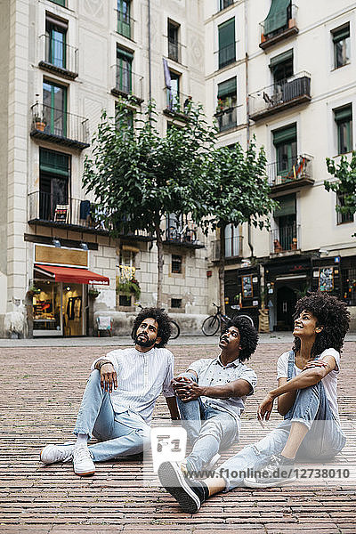 Spain  Barcelona  three friends sitting on a square looking up