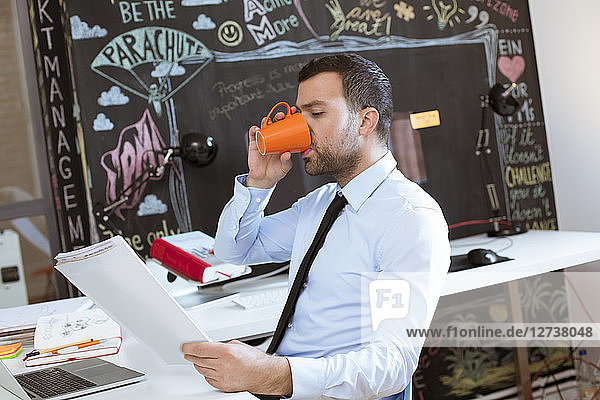 Businessman in creative office looking at documents and drinking coffee